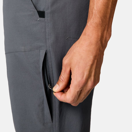 A hand is unzipping a pocket on Free Country Men’s Nylon Stretch Casual Trek Pant in gray, water-repellent fabric. The focus is on the hand and pocket, set against a plain light background.