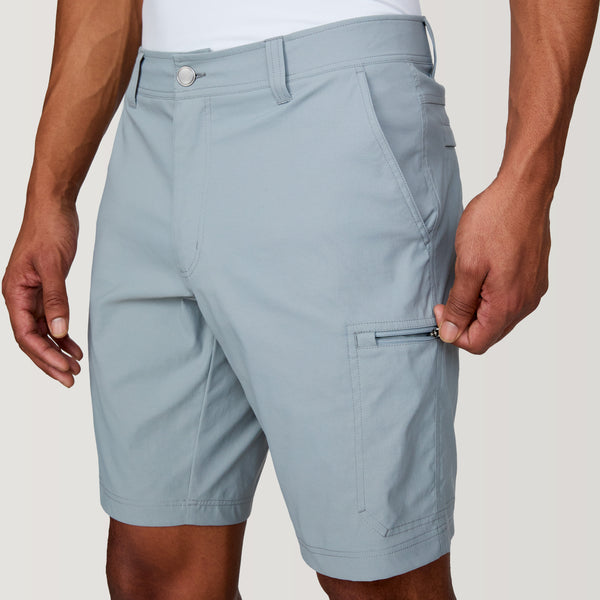 [Josiah is 6'3" wearing a size Medium.] Man wearing Free Country Men's Nylon Stretch Casual Short in Iron, size M, made from lightweight stretch performance fabric featuring a water repellent finish, slanted side pockets, and side leg zippered coin pocket, styled with a white t shirt and white shoes #color_iron