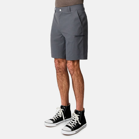 A person wears Free Country Men's Nylon Stretch Casual Short in gray with a zipper pocket, paired with a brown shirt and black high-top sneakers with white laces, standing against a plain white background.