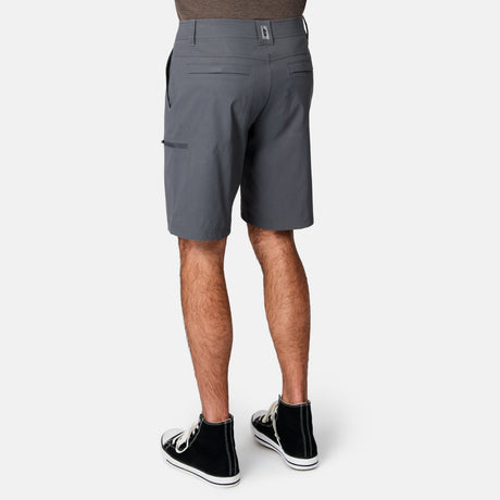 A person wearing Free Country Men's Nylon Stretch Casual Short in gray, knee-length, and black high-top sneakers stands with their back to the camera against a plain white background.