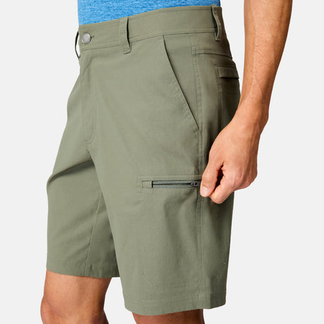 A person wears Free Country Men's Nylon Stretch Casual Short in olive green with a zippered side pocket and a blue shirt, shown close-up waist to knee. The hand holds the zipper, highlighting the shorts’ everyday convenience.