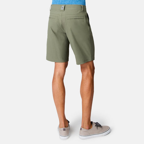 A person is seen from the back against a white background, wearing Free Country Men's Nylon Stretch Casual Short in light olive green, paired with a blue shirt and gray sneakers.