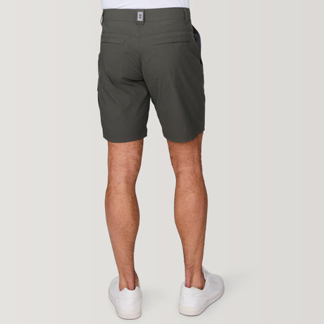 [Model is wearing a size Medium.] Man wearing Free Country Men's Nylon Stretch Trek Short in Olive, size M, made from lightweight stretch performance fabric featuring a water repellent finish, an adjustable waist belt, two back welt pockets, and two side sipper pockets, styled with a white t shirt and white shoes #color_olive