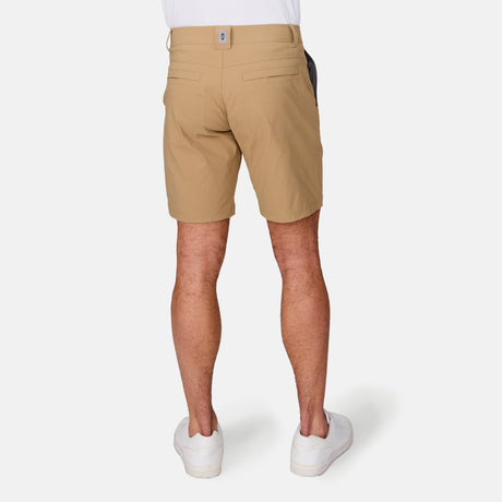 A person is seen from the back in a white shirt, white sneakers, and Free Country Men's Nylon Stretch Trek Shorts in tan with an adjustable waist belt, standing against a plain white background.
