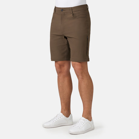 [Model is wearing a size Medium.] Man wearing Men's Nylon Stretch Convertible Pant in Saddle, size M, made from lightweight stretch performance fabric featuring a water repellent finish, an elastic waistband, above knee removable pants legs, and two side sipper pockets, styled with a grey t shirt and white shoes #color_saddle