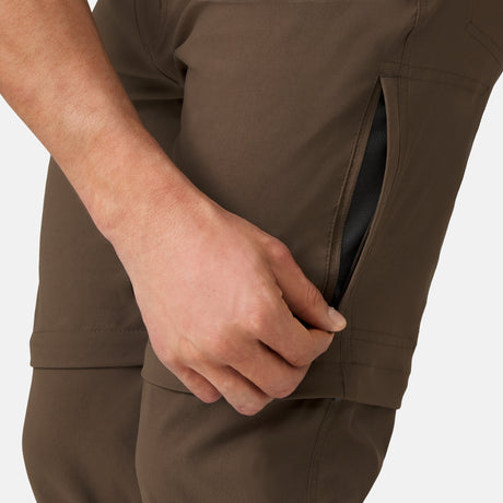 [Model is wearing a size Medium.] Man wearing Men's Nylon Stretch Convertible Pant in Saddle, size M, made from lightweight stretch performance fabric featuring a water repellent finish, an elastic waistband, above knee removable pants legs, and two side sipper pockets, styled with a grey t shirt and white shoes #color_saddle