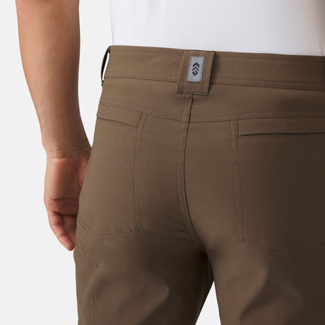 [Model is wearing a size Medium.] Man wearing Men's Nylon Stretch Convertible Pant in Saddle, size M, made from lightweight stretch performance fabric featuring a water repellent finish, an elastic waistband, above knee removable pants legs, and two side sipper pockets, styled with a grey t shirt and white shoes #color_saddle