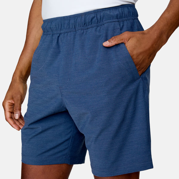 [Anderson is 6'2" wearing a size Medium.]  Man wearing the Free Country Men's Boardwalk Woven Pull-On Trek Short in Denim, size M, made from lightweight breathable polyester fabric and featuring an elastic waistband and slanted pockets, styled with a white t shirt #color_ denim