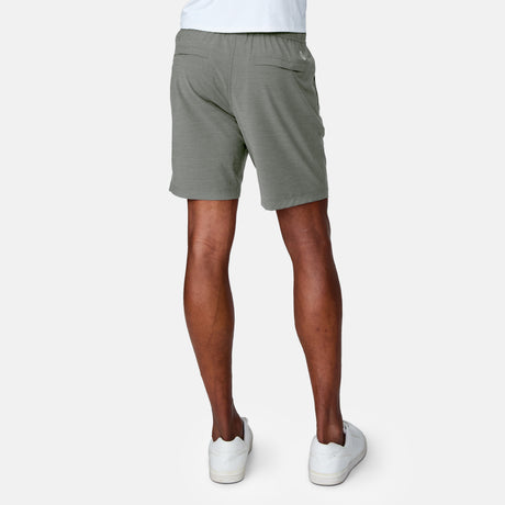 Only the lower half of a person is visible as they stand facing away from the camera, wearing Clearance Men's Trek Short in light green and white sneakers against a plain, light background.