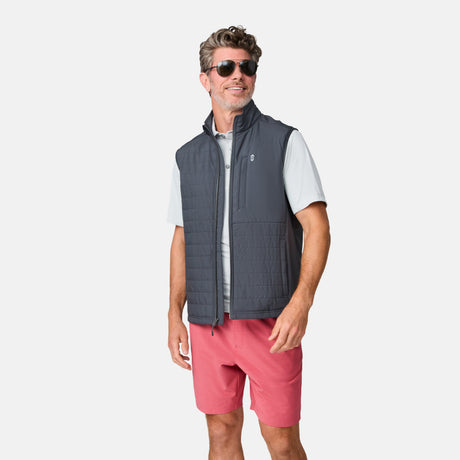 Man wearing sunglasses, a gray zip-up vest over a light gray short-sleeve shirt, and Clearance Men’s Trek Short in pink stands smiling against a plain white background.