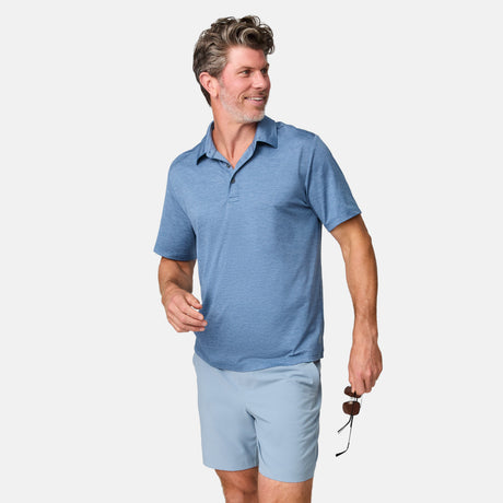 A smiling gray-haired man wears a light blue polo and Clearance Men’s Trek Short made of breathable fabric, holding sunglasses in his right hand against a white background.