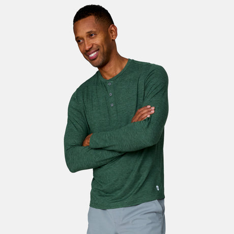 [Anderson is 6'2" wearing a size Medium.] Man wearing Free Country Men's Henley Long Sleeve Shirt in Cilantro, size M, made from lightweight soft polyester fabric featuring a classic fit with anti odor and upf technology, styled with grey shorts #color_cilantro