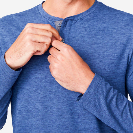 [Miguel is 6'2" wearing a size Medium.] Man wearing Free Country Men's Henley Long Sleeve Shirt in Steel Blue, size M, made from lightweight soft polyester fabric featuring a classic fit with anti odor and upf technology, styled with brown shorts #color_steel-blue