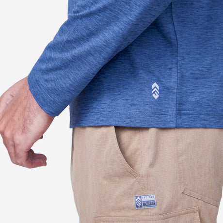 [Miguel is 6'2" wearing a size Medium.] Man wearing Free Country Men's Henley Long Sleeve Shirt in Steel Blue, size M, made from lightweight soft polyester fabric featuring a classic fit with anti odor and upf technology, styled with brown shorts #color_steel-blue