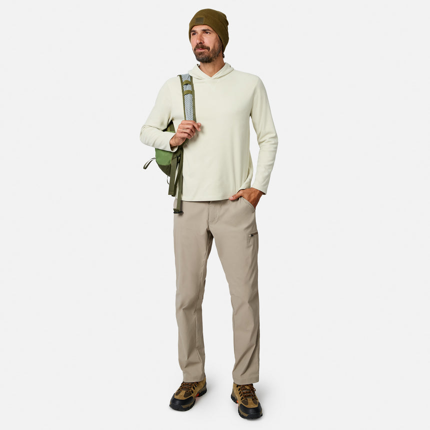 [Model is wearing size M.] A man modeling a light beige hooded long-sleeve shirt, khaki pants, brown hiking boots, and an olive green beanie, carrying a green backpack strap against a light gray studio background.