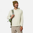 [Model is wearing size M.] A man wearing a light cream hooded sweatshirt, olive green beanie, and khaki pants, carrying an olive green backpack over his shoulder against a light gray studio background.