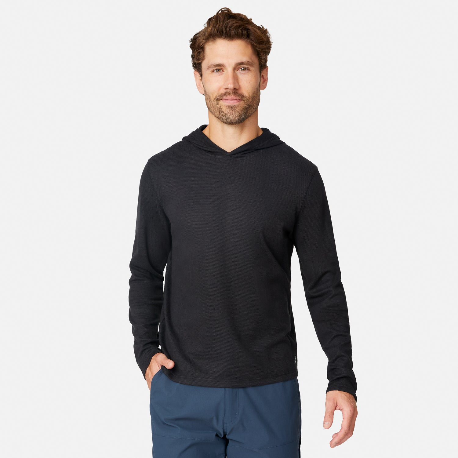 [Model is wearing size M.] A man wearing a black long-sleeve hooded shirt and blue pants, standing against a light gray studio background.