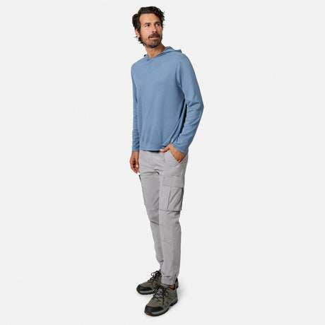 [Model is wearing size M.] A man wearing a dusty blue long-sleeve hooded shirt, light gray cargo pants, and hiking boots, standing against a solid off-white background.