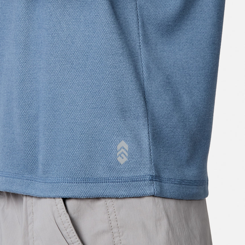 [Model is wearing size M.] Close-up of a blue textured athletic top with a small white logo near the hem, paired with light gray shorts against a clean white background.