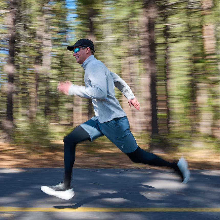 A man wearing the Free Country Men’s Twill Interlock 1/4 Zip Long Sleeve Shirt runs swiftly along a road through a forest, with motion blur in the background emphasizing his speed.