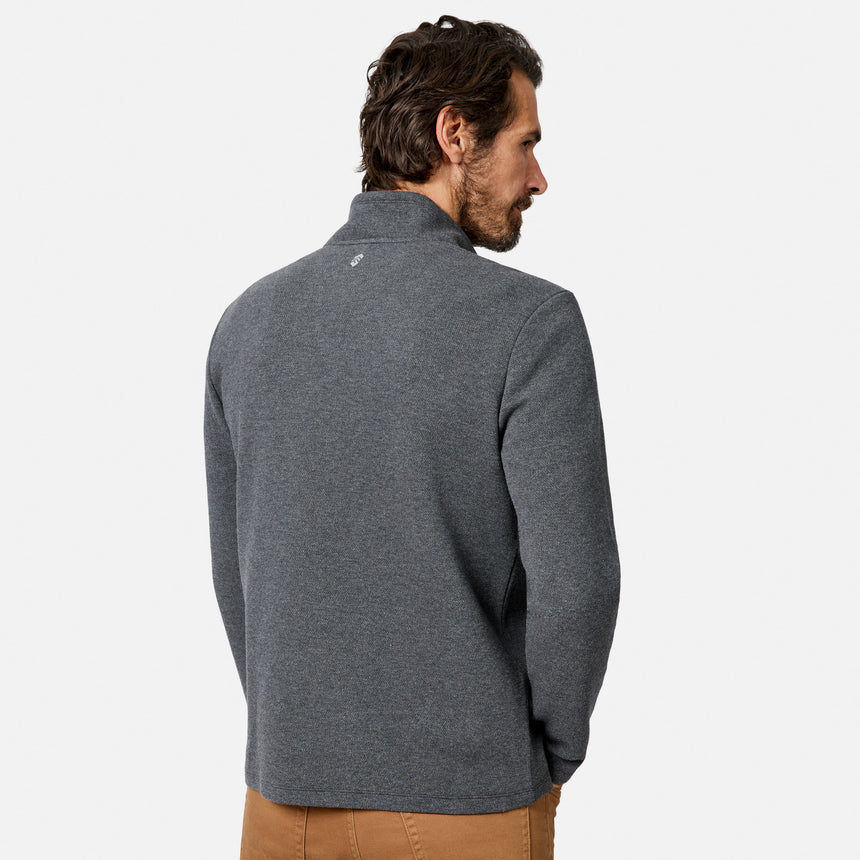A man with dark hair, wearing a Free Country Men’s Twill Interlock 1/4 Zip Long Sleeve Shirt in gray and tan twill interlock pants, stands facing away with his hands in his pockets against a plain white background.