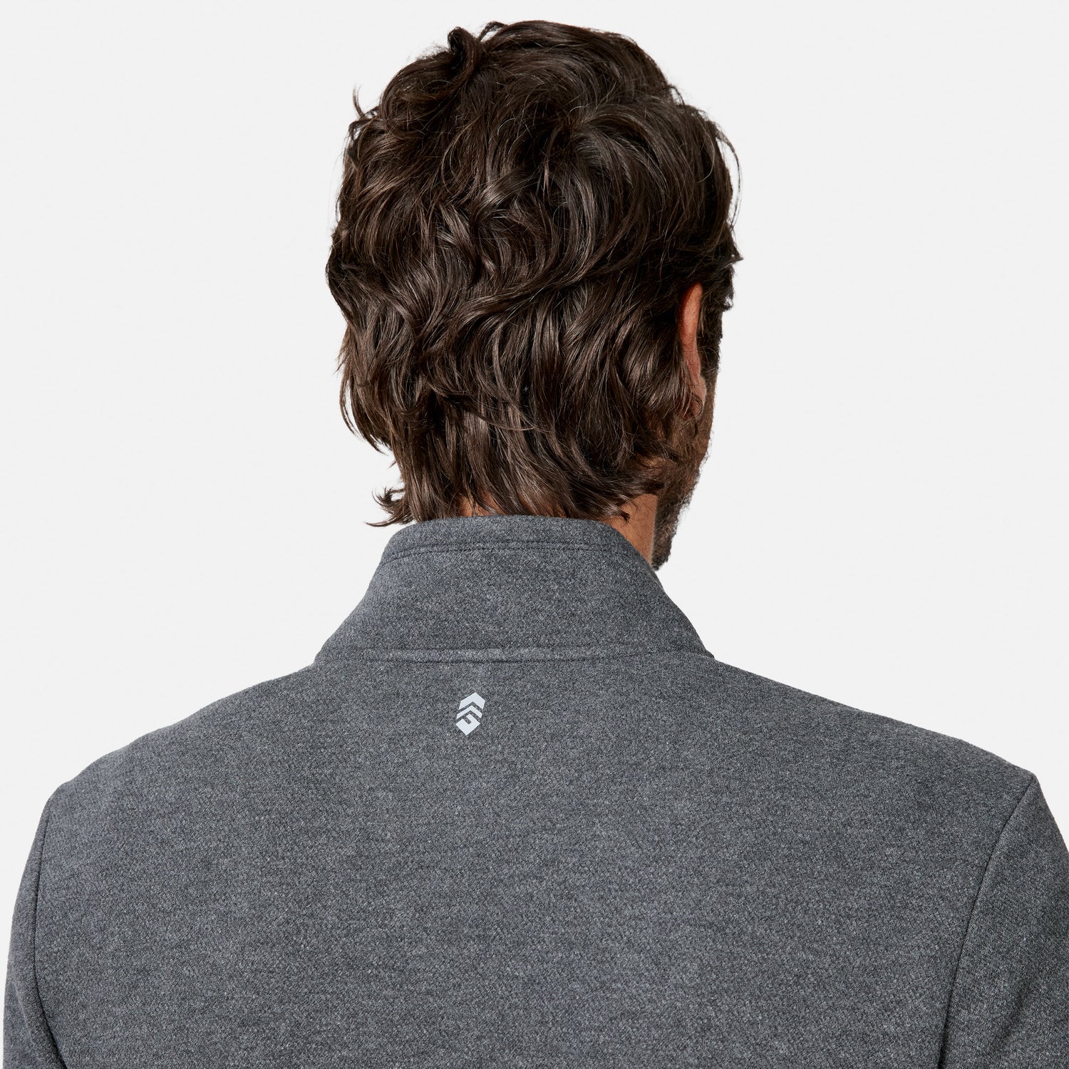 A person with wavy brown hair is shown from behind, wearing the Free Country Men’s Twill Interlock 1/4 Zip Long Sleeve Shirt in gray, which features a small white logo on the back of the collar. The breathable knit fabric enhances comfort, and the background is plain white.