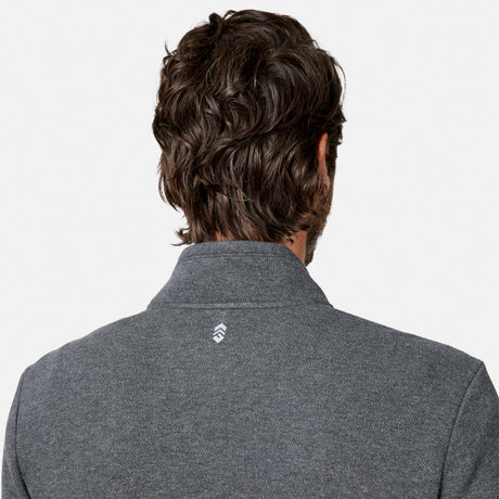 A person with wavy brown hair is shown from behind, wearing the Free Country Men’s Twill Interlock 1/4 Zip Long Sleeve Shirt in gray, which features a small white logo on the back of the collar. The breathable knit fabric enhances comfort, and the background is plain white.