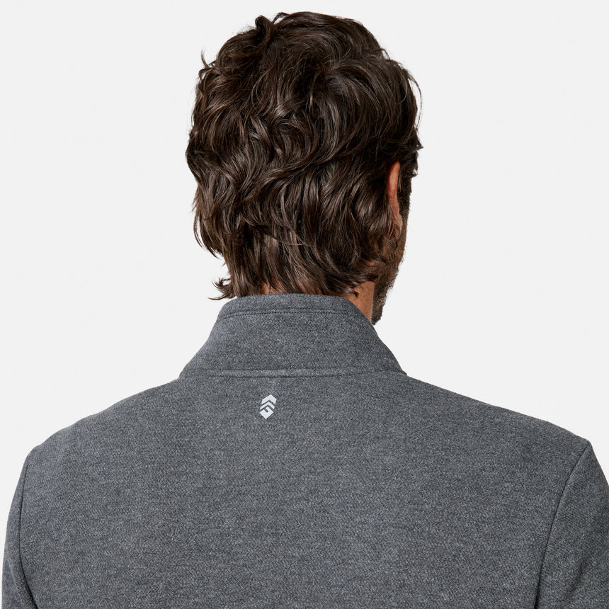 A person with wavy brown hair is shown from behind, wearing the Free Country Men’s Twill Interlock 1/4 Zip Long Sleeve Shirt in gray, which features a small white logo on the back of the collar. The breathable knit fabric enhances comfort, and the background is plain white.