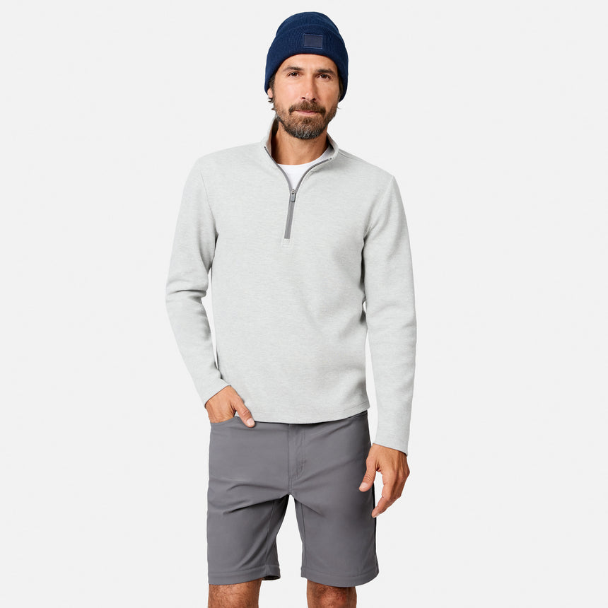 A man wears the Free Country Men’s Twill Interlock 1/4 Zip Long Sleeve Shirt in Grey Heather, paired with gray shorts and a navy blue beanie, standing against a plain white background.