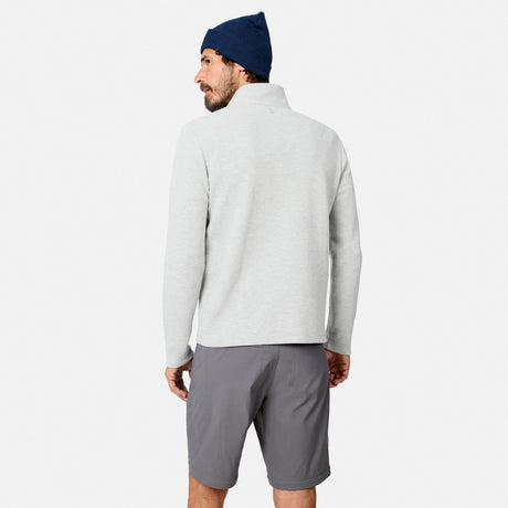A man stands facing away against a plain white background, wearing a light gray Men’s Twill Interlock 1/4 Zip Long Sleeve Shirt by Free Country, paired with dark gray shorts and a navy beanie.