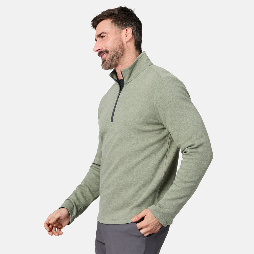 A man stands sideways and smiles against a plain white background, wearing the Free Country Men’s Twill Interlock 1/4 Zip Long Sleeve Shirt in light green, crafted from breathable knit fabric, paired with gray pants.
