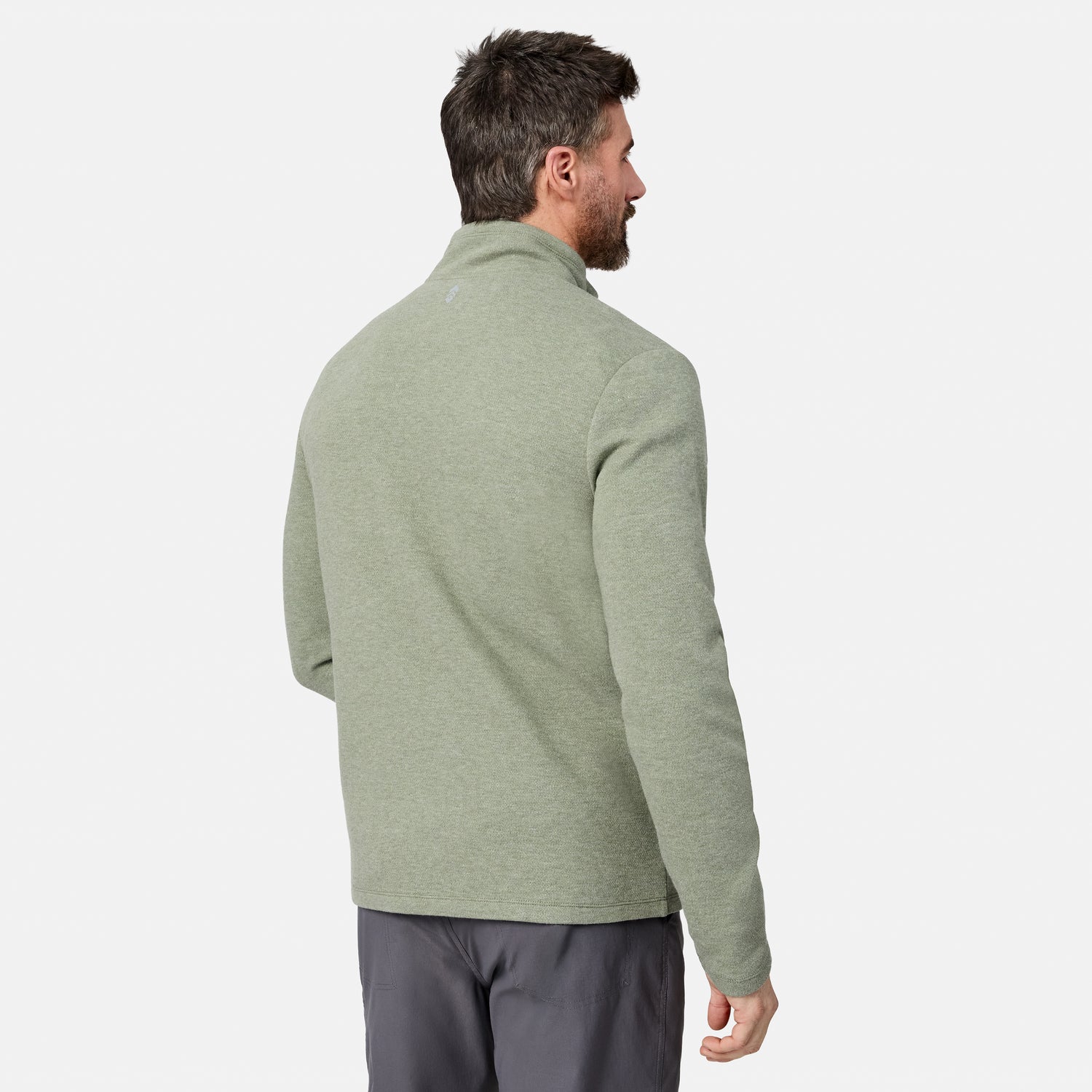 A man with short dark hair, standing and facing away from the camera against a plain white background, is wearing gray pants and a light green Men’s Twill Interlock 1/4 Zip Long Sleeve Shirt by Free Country.