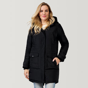 A woman with long blonde hair wears the Clearance Women's Arctic Anorak Jacket—a black eco-friendly hooded winter coat with REPREVE fill and front pockets—paired with blue jeans, standing against a plain light gray background.