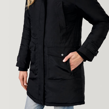 A person wears the Clearance Women's Arctic Anorak Jacket—a long black eco-friendly coat with REPREVE fill, snap buttons, and front pockets—paired with light blue jeans against a plain light background.