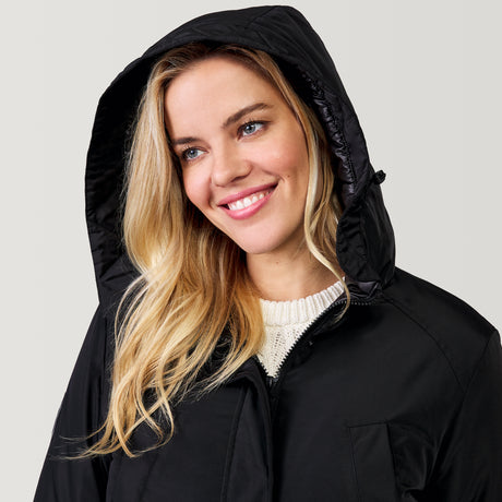 A woman with long blonde hair smiles while wearing the Clearance Women’s Arctic Anorak Jacket with REPREVE fill over a white sweater, looking slightly to the side against a plain light background.