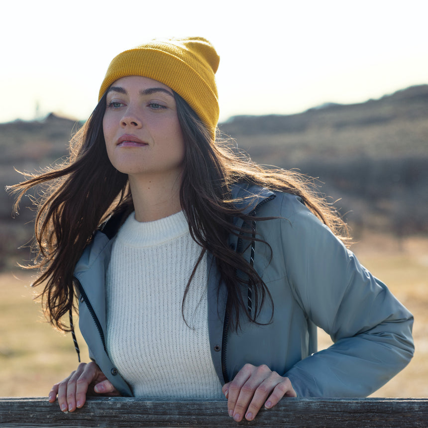 Woman wearing a yellow beanie and light green jacket in a natural setting