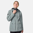 [CJ is 5'10" wearing size S.] Women’s light green hooded rain jacket with front zip closure, flap pockets with button accents, black hood drawstrings, and a sleeve patch—layered over a dark gray turtleneck and styled with black pants for a sleek, weather-ready look.