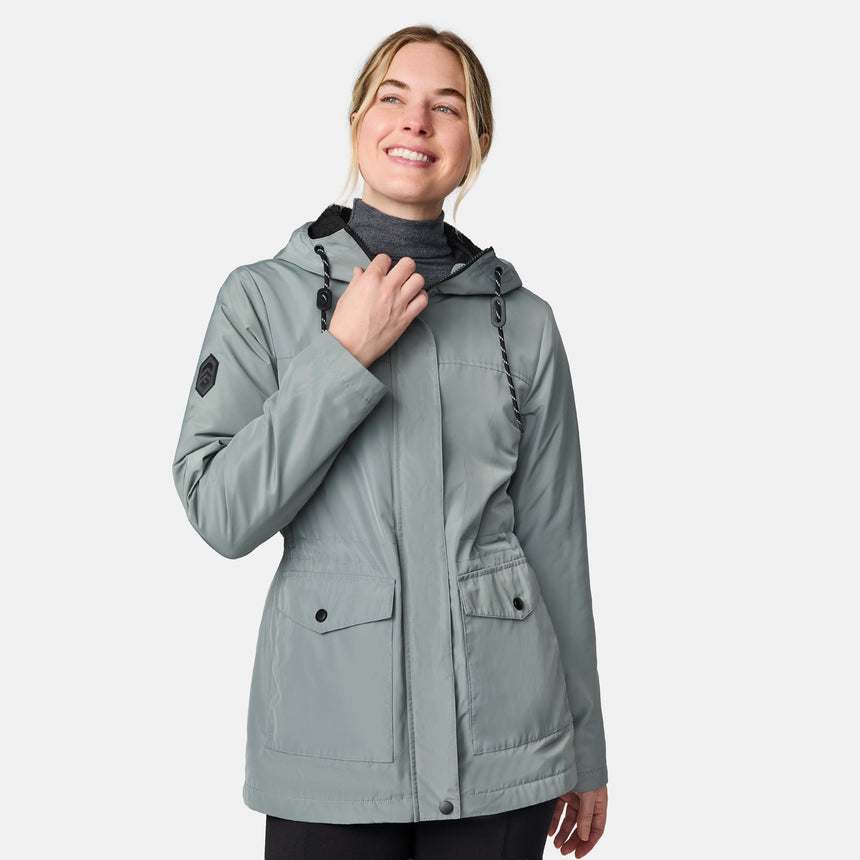 [CJ is 5'10" wearing size S.] Women’s light green hooded rain jacket with front zip closure, flap pockets with button accents, black hood drawstrings, and a sleeve patch—layered over a dark gray turtleneck and styled with black pants for a sleek, weather-ready look.