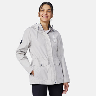 A woman in the Free Country Women's Rain Away Anorak Rain Jacket, light gray with an adjustable hood and pockets, smiles with her hands in the pockets while looking slightly up against a plain white background.