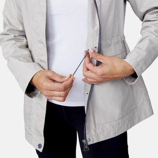 A person adjusts the elastic drawstring inside a partially unzipped Women's Rain Away Anorak Rain Jacket by Free Country, revealing a white shirt underneath. Only their torso and hands are visible.
