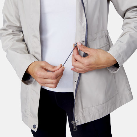 A person adjusts the elastic drawstring inside a partially unzipped Women's Rain Away Anorak Rain Jacket by Free Country, revealing a white shirt underneath. Only their torso and hands are visible.