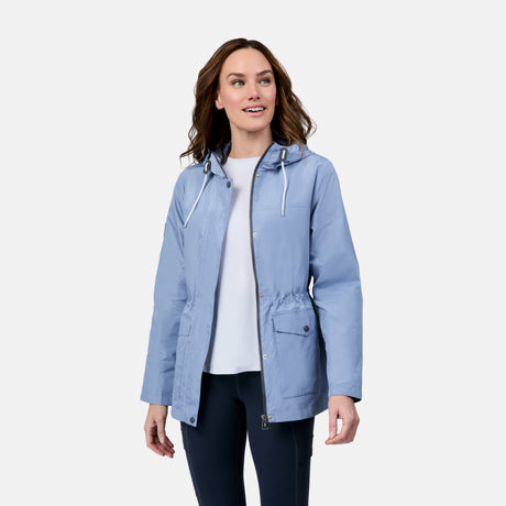 A woman smiles and looks to the side while wearing the Free Country Women's Rain Away Anorak Rain Jacket in light blue over a white shirt and dark pants, standing against a plain white background.