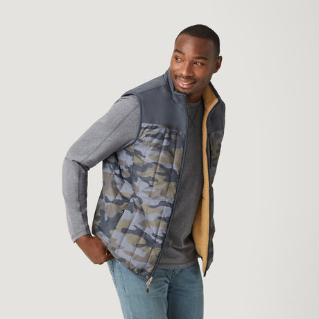 A man in a gray long-sleeve shirt, blue jeans, and the Clearance Men's FreeCycle® Alpine Reversible Vest with recycled polyfill and tan lining stands smiling, looking right against a plain white background.
