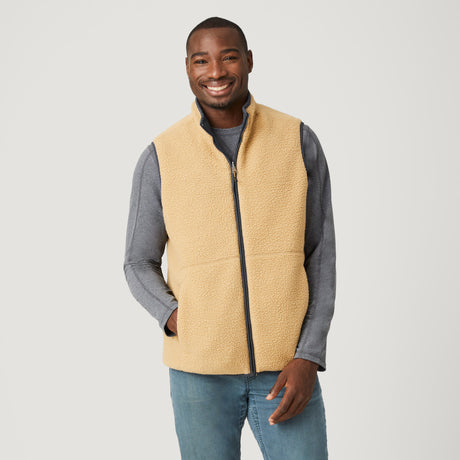 A man smiles against a plain background, wearing the Clearance Men's FreeCycle® Alpine Reversible Vest over a gray long-sleeve shirt and light blue jeans, with one hand in his pocket.