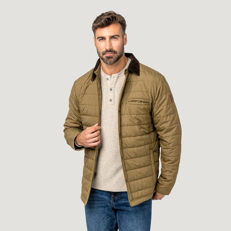 [Model is wearing size M.] A man wearing a tan quilted puffer jacket with a dark brown collar, layered over a beige henley shirt and blue jeans, set against a solid light gray background.