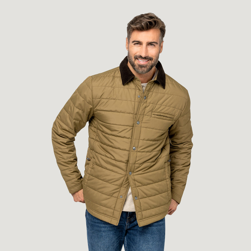 [Model is wearing size M.] A man wearing a tan quilted jacket with a dark brown corduroy collar, paired with a cream shirt and blue jeans, standing against a solid light gray background.