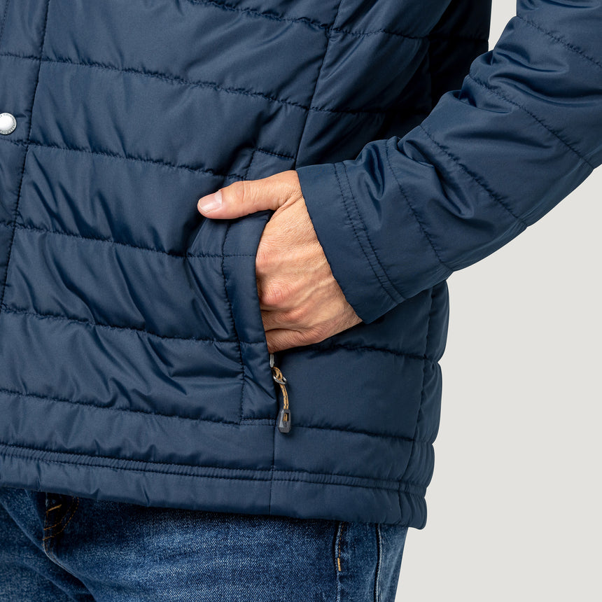 [Model is wearing size M.] Close-up of a person wearing a navy blue quilted puffer jacket with a side zip pocket, hand in pocket, and blue jeans against a light gray background.