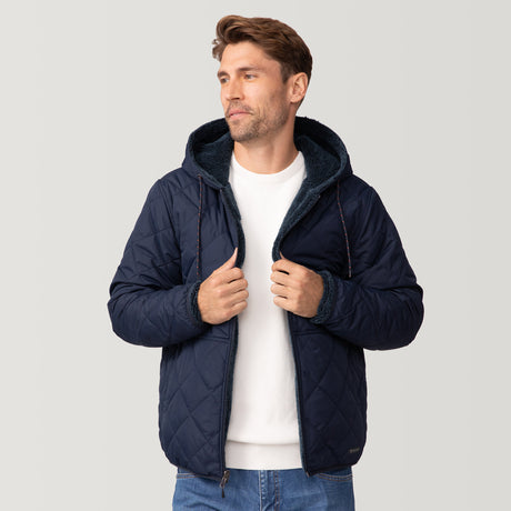 [Matt is 6'2" wearing a size Medium.] Men’s Free Country reversible quilted jacket in navy with zip-front closure, adjustable drawstring hood, and dual hand pockets—flips to plush sherpa interior for added warmth and comfort. Styled with a white crewneck shirt and jeans for a casual, cold-weather look.