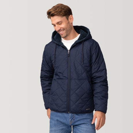 [Matt is 6'2" wearing a size Medium.] Men’s Free Country reversible quilted jacket in navy with zip-front closure, adjustable drawstring hood, and dual hand pockets—flips to plush sherpa interior for added warmth and comfort. Styled with a white crewneck shirt and jeans for a casual, cold-weather look.