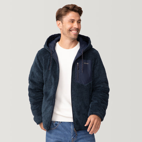 [Matt is 6'2" wearing a size Medium.] Men’s Free Country reversible quilted jacket in navy with zip-front closure, adjustable drawstring hood, and dual hand pockets—flips to plush sherpa interior for added warmth and comfort. Styled with a white crewneck shirt and jeans for a casual, cold-weather look.